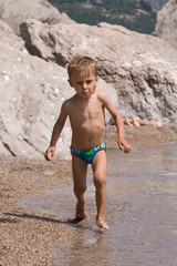 little a boy hurries on water on a background rocky mountains