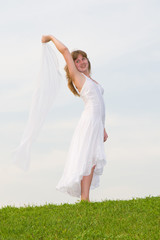 Fototapeta na wymiar Girl with a white scarf in a hand stands on a green grass