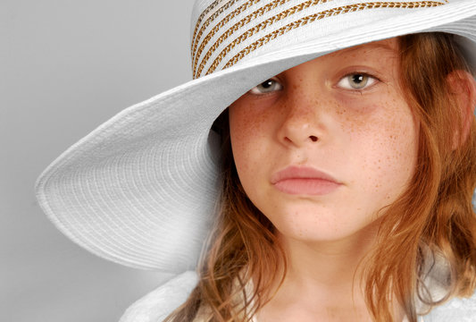 Young freckle faced girl with serious look wearing big hat