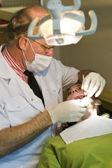 A mature dentist working on a lady patient.