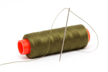 Spool of olive green thread and needle on white background.