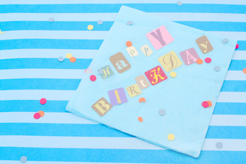 Happy birthday cut out letters on blue napkin with confetti