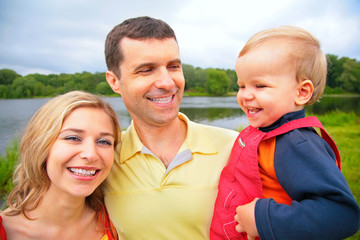 Mother and father with child on hands outdoors. wide angle.