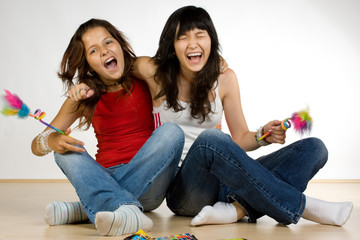 Two teenage girls laughing and sitting on the floor.