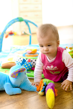 Baby girl (9 months) playing with soft toys at home.