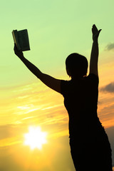 female praying with bible against summer sunset,