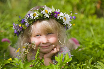 happy little girl in flowers wreath lying on green meadow