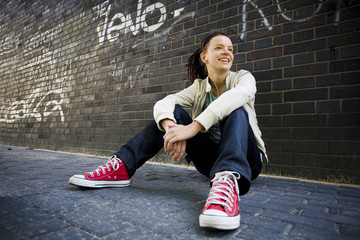 Young woman sitting against a brick wall