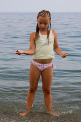 little girl stands in water ashore