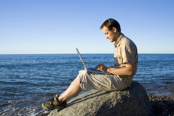 Mann mit Laptop am Strand