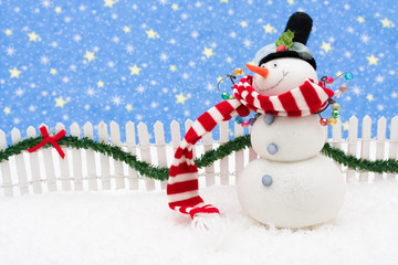 Fototapeta premium Snowman and white picket fence with green garland