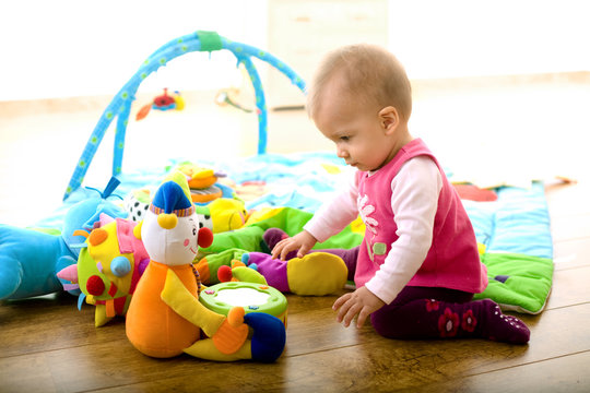 Baby girl (9 months) playing with soft toys at home.