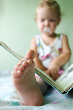 An image of a baby reading a book. Foot closeup