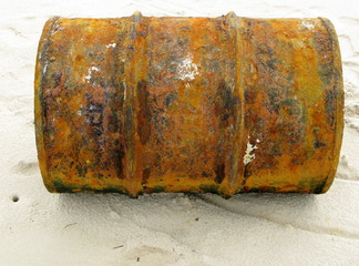Bidon de pétrole rouillé échoué sur une plage.
