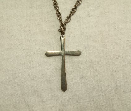 Plain Christian cross on chain against white sweater.