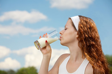 The woman drinks milk against the blue sky