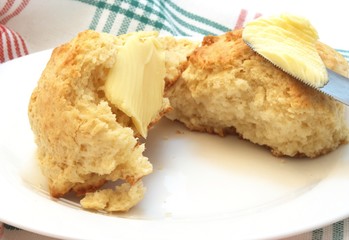 Homemade buttered scones on white plate and knife with butter.