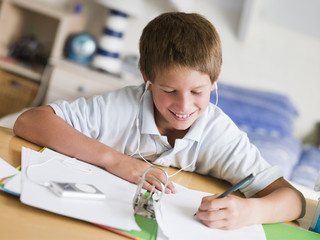Naklejka premium Young Boy Doing His Homework While Listening To Music On MP3