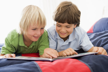 Two Young Boys Lying Down On A Bed Reading A Book
