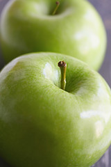Two green granny smith apples, with focus on front apple stem.