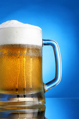 Mug of beer close-up with froth over blue background