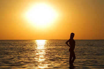 Fototapeta premium Silhouette of the young woman on a sea bay on a sunset