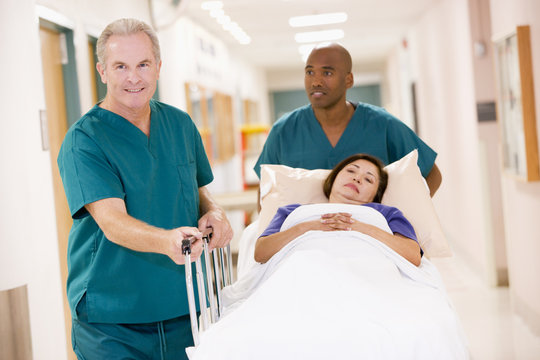 Two Orderlies Pushing A Woman In A Bed Down A Hospital Corridor