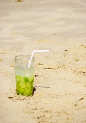 Verre de caïpirinha et paille sur le sable de la plage.
