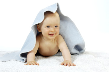 Hübsches Baby lachend unter blauen Decke nach vorne schauend