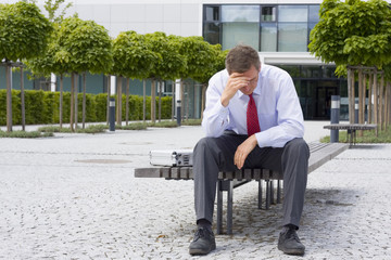 Frustrierter Geschäftsmann sitzt auf Bank vor Bürogebäude