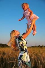 Mother raises child on hands in wheaten field