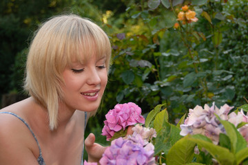 Obraz na płótnie Canvas young blond girl in garden smelling flower
