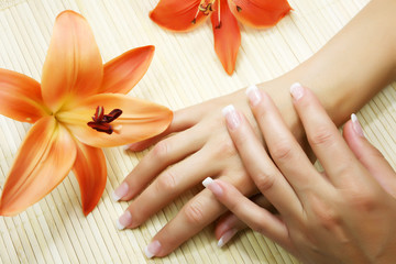 Beautiful hands with a good manicure lie near bright lilies