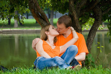 Fototapeta premium Loving couple kisses under a tree on a river bank
