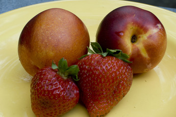 Two strawberries and two nectarines on a yellow plate