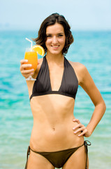 A young woman on the beach with a glass of orange juice