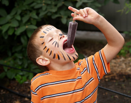 young boy with tiger face paint eating a frozen ice treat