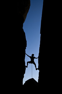 Rock climber silhouetted as he climbs up a chimney.