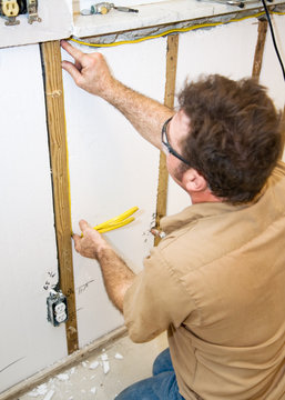 Electrician installing wiring in an interior wall.