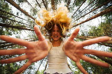 Agressive woman stretch her hands to camera at piny forest