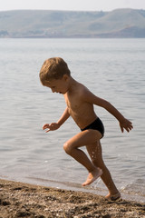 the little boy runs out from water at lake against mountains