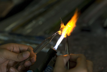 Artist shaping hot glass into a figurine, using a gass flame.