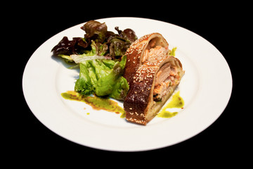 Salmon strudel on a white plate isolated on black