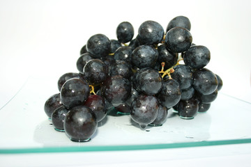 Black grapes with water drops on the plate.
