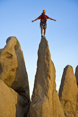 A climber silhouetted on the summit of a rock spire.