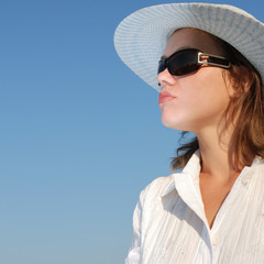 The woman in glasses and a hat on a background of the sky