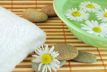 Towel, bowl with daisy and spa stone on the mat