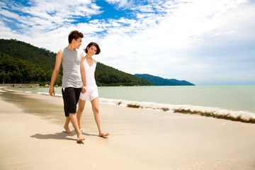 asian young couple holding hands walking along the beach