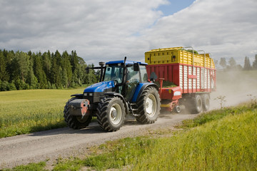 big blue tractor with a red trailer on rural road - 9527914