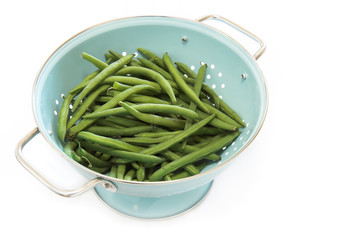 A blue colander full of green beans, isolated on white.